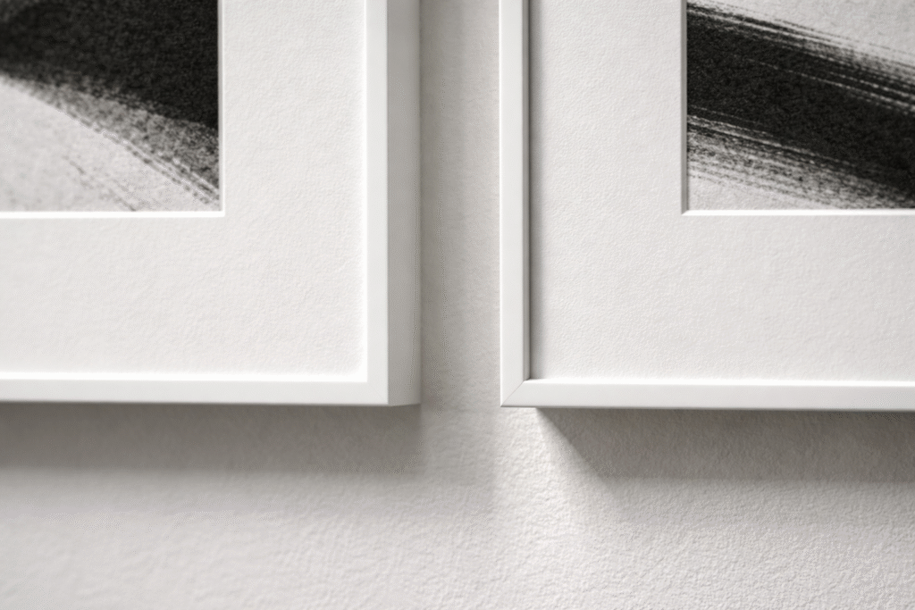 Close-up detail of two white museum frames perfectly aligned on a gallery wall for exhibition printing.